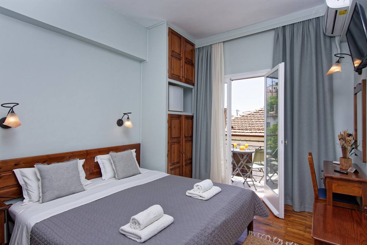 Een hotelkamer met een bed, houten hoofdbord, grijze beddengoed, twee bedlampen, een houten bureau en een stoel.