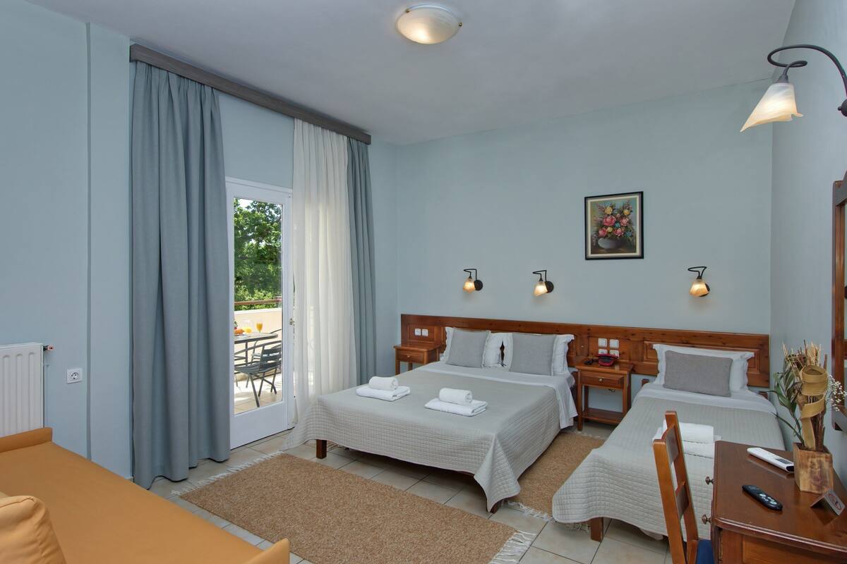 Een hotelkamer met twee bedden, een bank, een eettafel en uitzicht op het omliggende landschap.