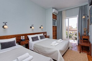 A hotel room with two beds, a wooden headboard, bedside tables with lamps, a view through a glass door to an outdoor area, and a small table with a vase. - Hotel Katia (South Pelion)