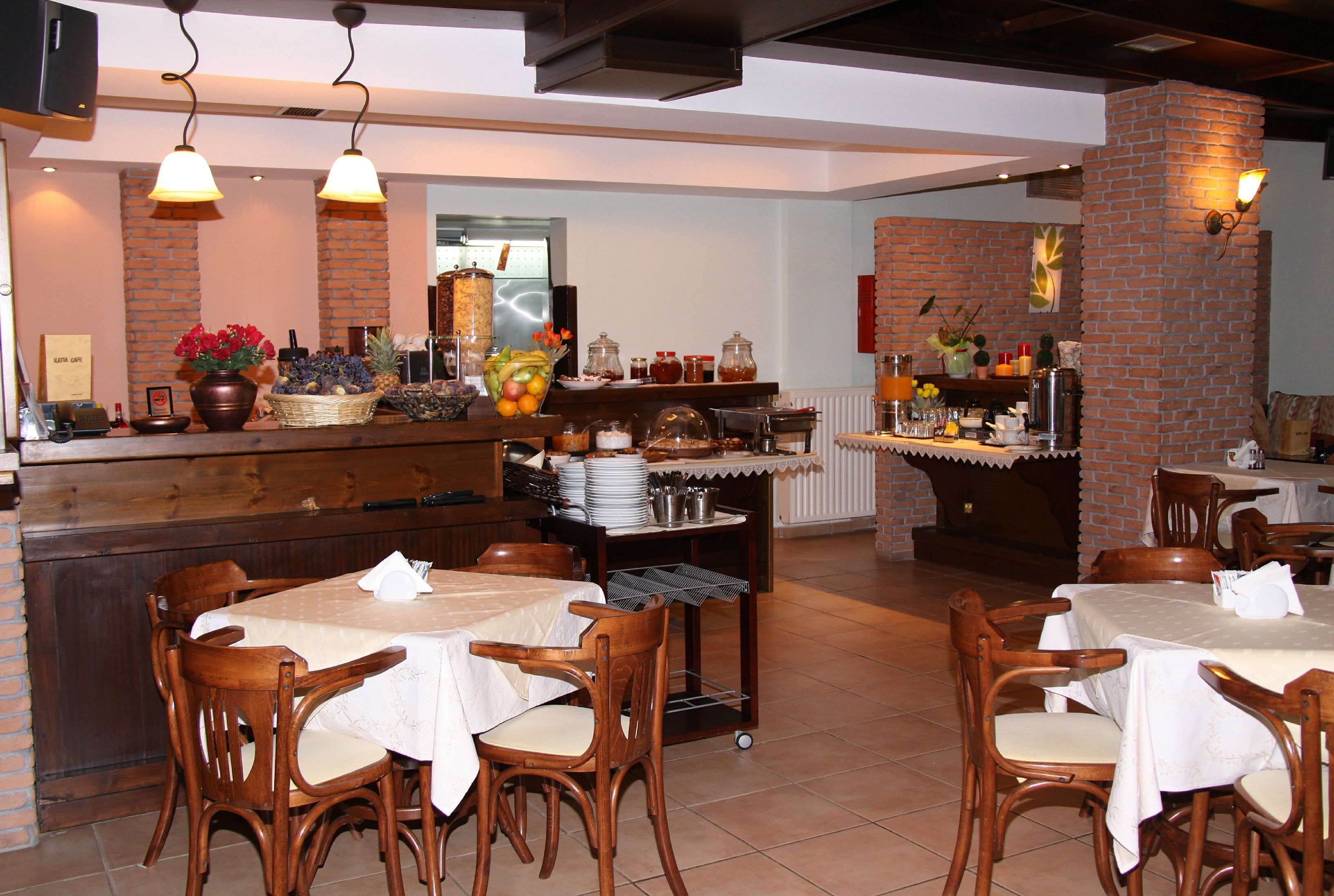A restaurant with brick walls, wooden tables, and chairs. There are various food items and condiments on the counter.