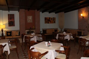 A restaurant with wooden tables and chairs, brick walls, and artwork on the walls. - Hotel Katia (South Pelion)