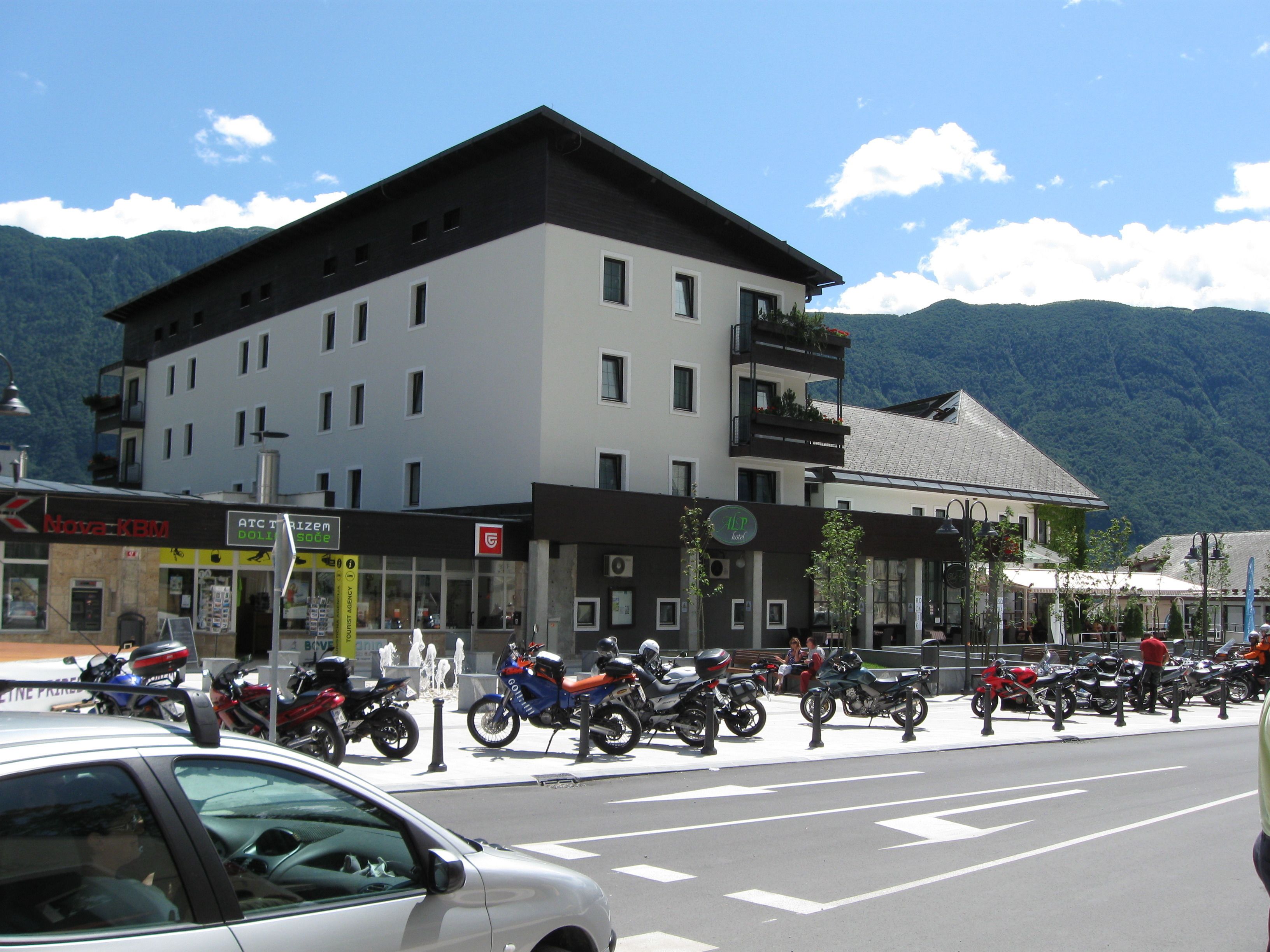 A hotel with multiple floors, a balcony on the upper level, and a mountain backdrop.