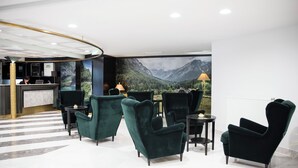 Un hall con mostrador de recepción, sillones verdes y un gran mural en la pared que representa un paisaje montañoso.