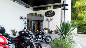 Entrada de un hotel con un letrero que dice "ALP hotel", dos motocicletas estacionadas al frente y plantas en macetas alrededor de la entrada.