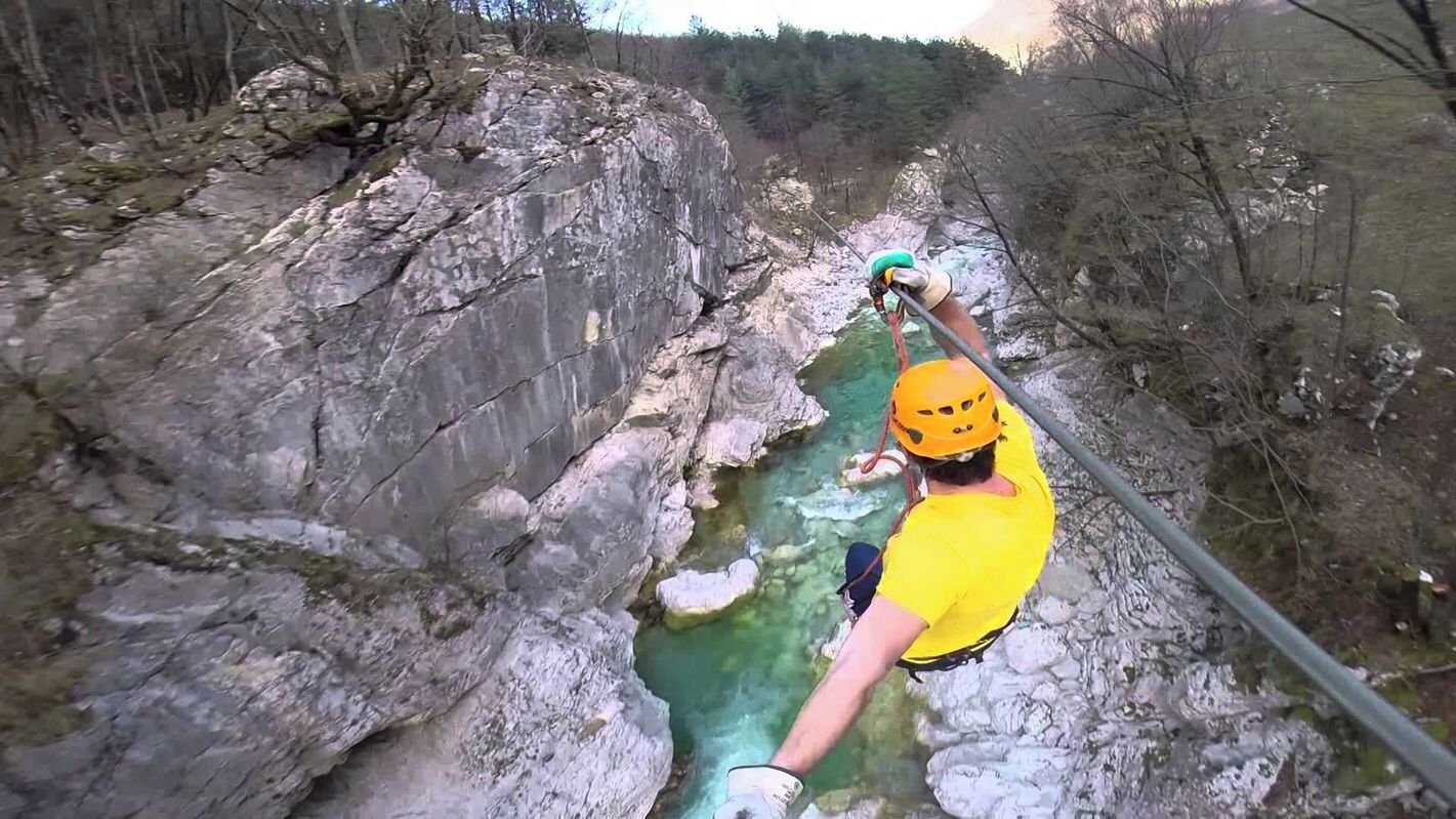 Una persona descendiendo en rappel por un acantilado rocoso hacia un río.