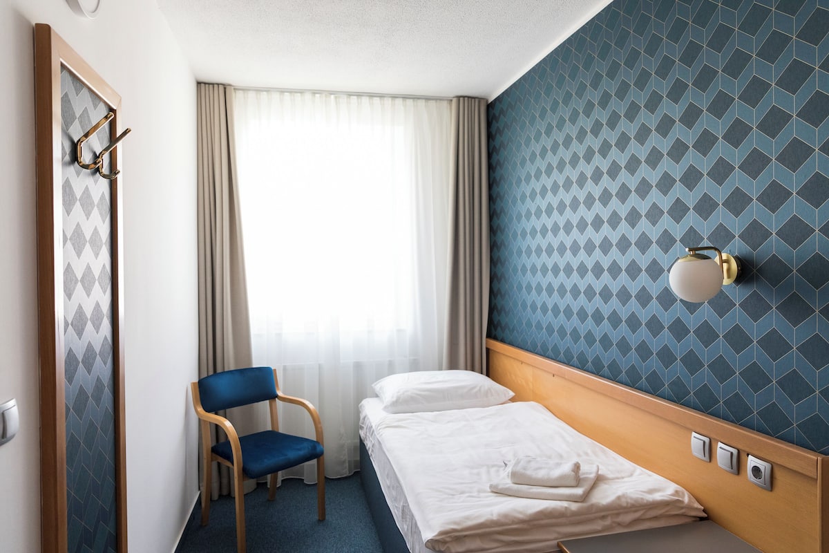 Habitación de hotel con cama, una silla, una lámpara de pared y una ventana con cortinas.