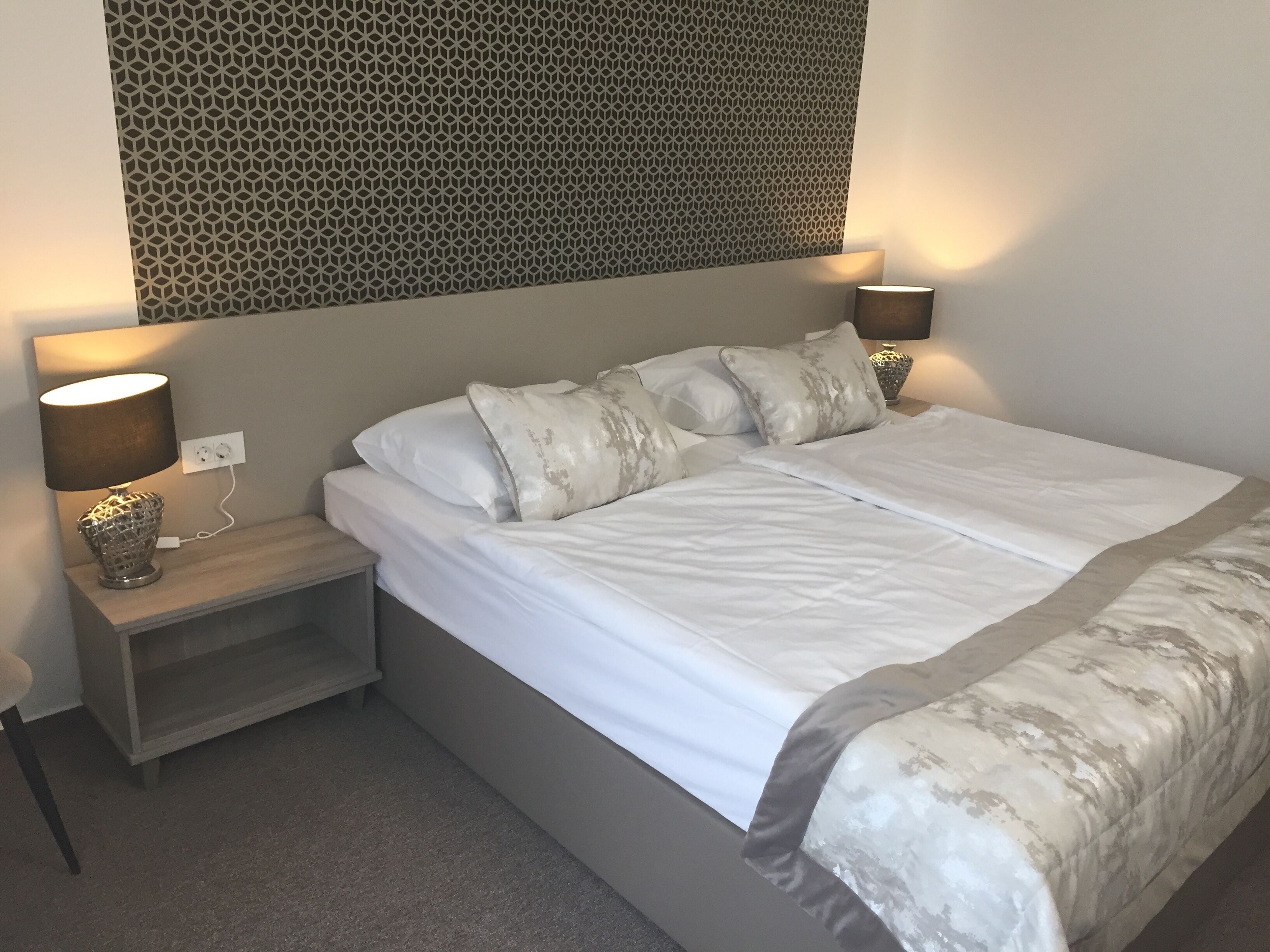 Una cama bien hecha con sábanas blancas, dos lámparas de noche y un papel tapiz decorativo sobre la cama.