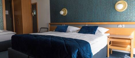 A hotel room with a large bed, a wooden nightstand, a wardrobe, and a wall-mounted mirror.