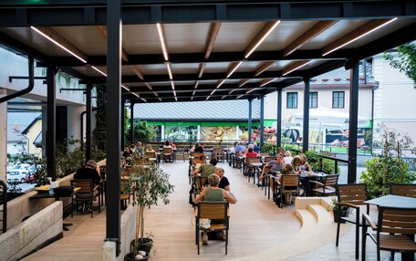 An outdoor café with wooden tables and chairs, surrounded by potted plants.