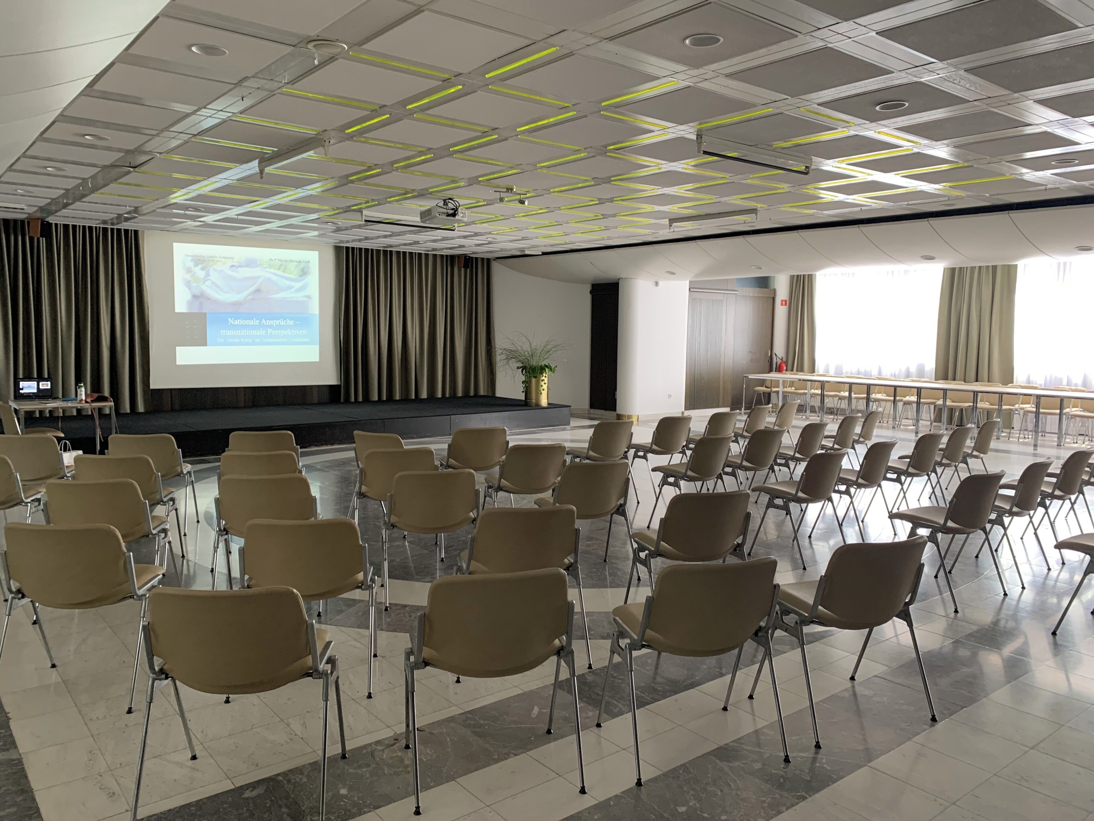 A conference room with rows of chairs, a projector screen, and a presentation on the wall.