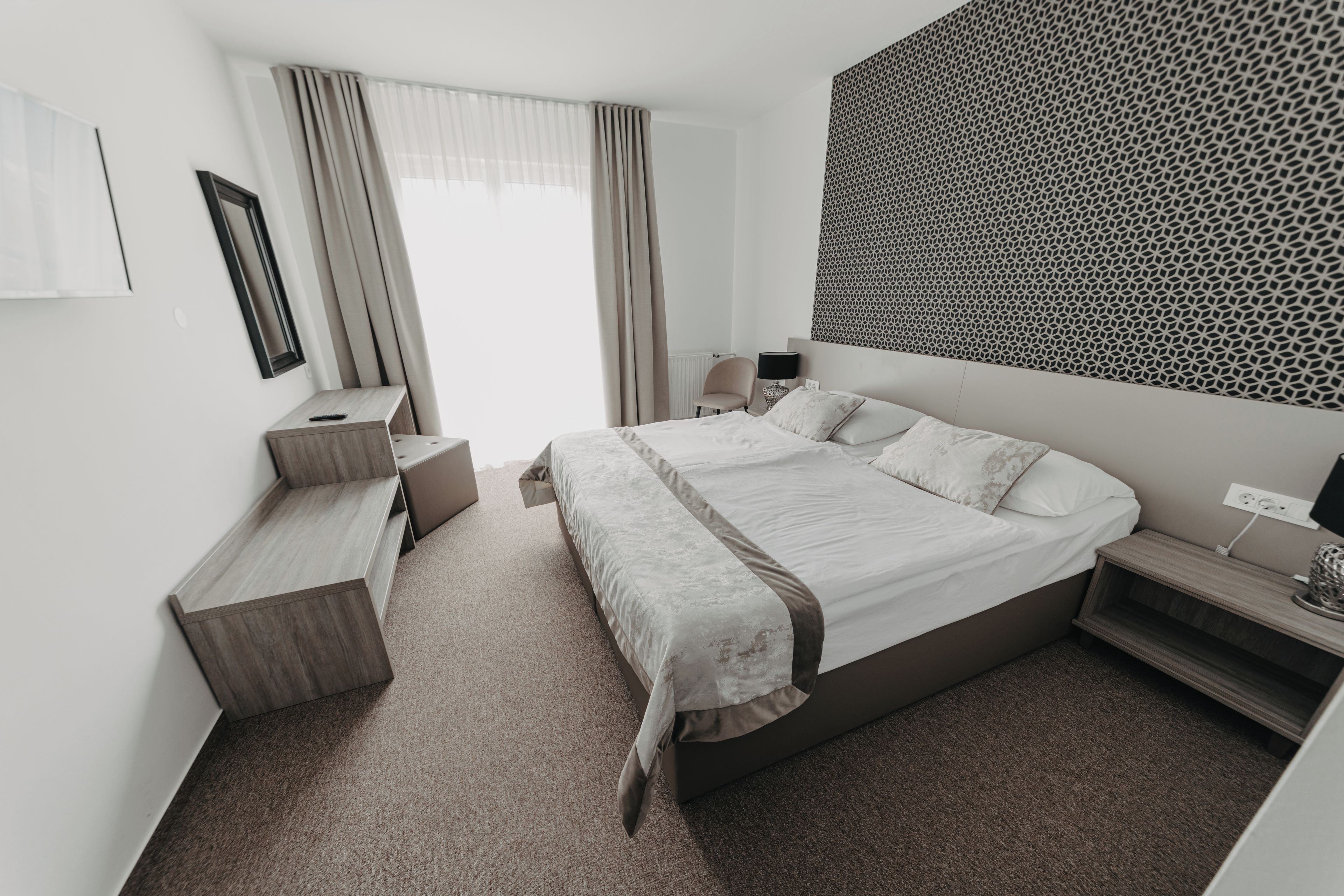Una habitación de hotel moderna con una cama grande, un escritorio, una silla y un papel tapiz estampado.