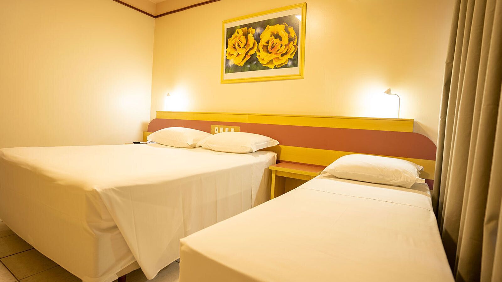 Habitación de hotel con dos camas individuales, una mesita de noche, una lámpara y un cuadro de flores en la pared.