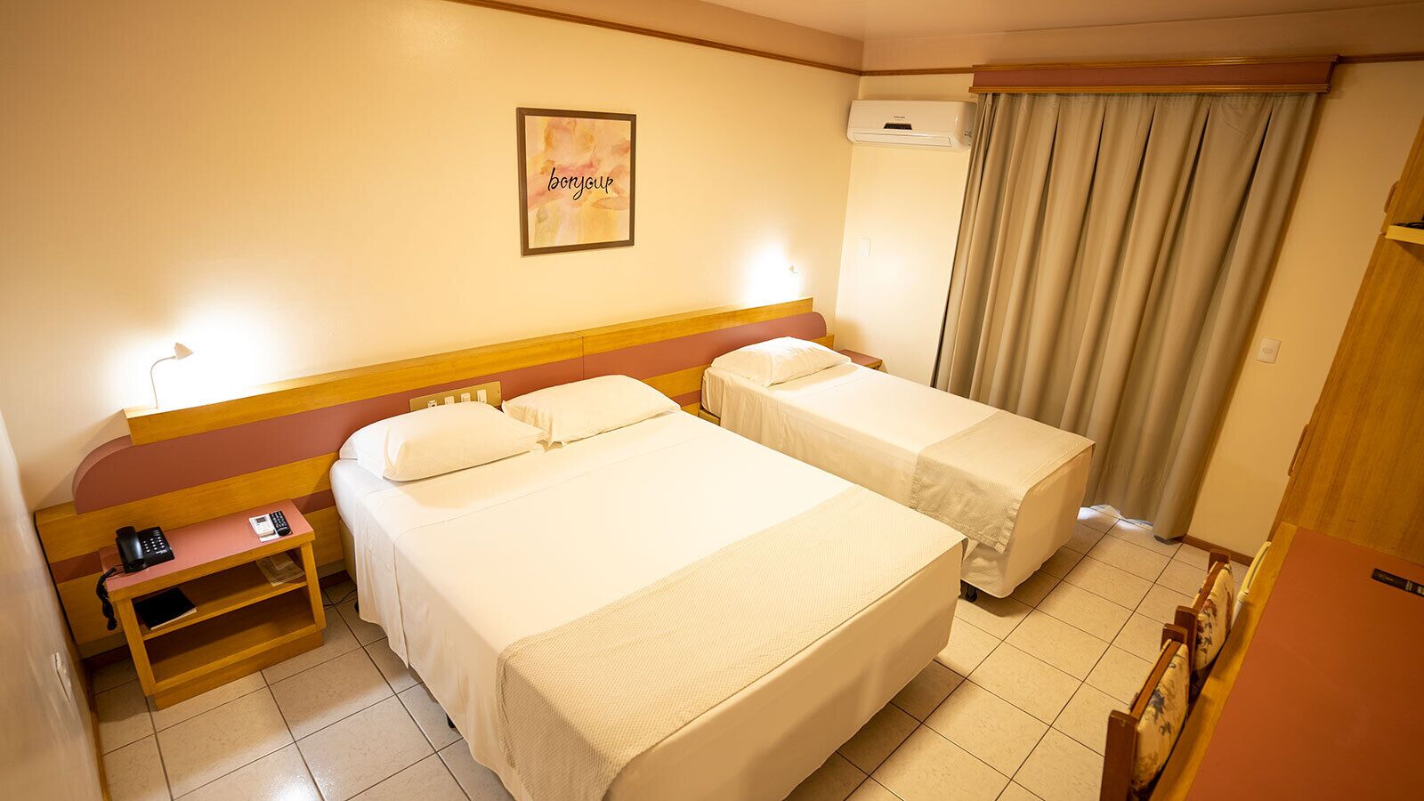 Habitación de hotel con dos camas, una mesita de noche con un teléfono, un equipo de aire acondicionado y una cortina.