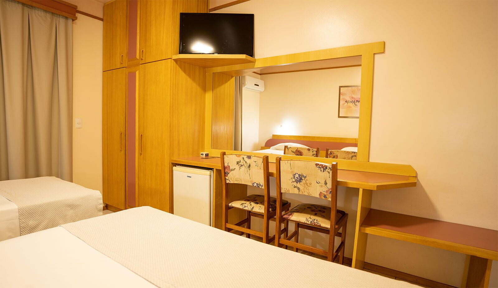 Habitación de hotel pequeña con una cama individual, un escritorio con silla, televisión y un refrigerador pequeño.