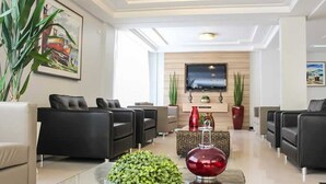 Una sala de estar moderna con sofás negros, una mesa de centro de vidrio y un televisor de pantalla plana montado en la pared.