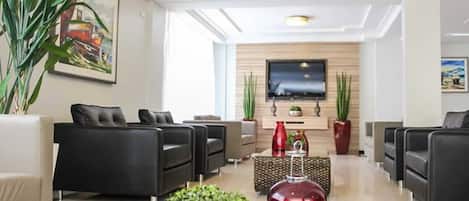 A modern living room with black sofas, a glass coffee table, and a flat-screen TV mounted on the wall.