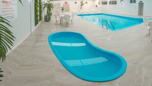 Una piscina con cubierta azul, rodeada de sillas y mesas blancas, y plantas de interior.