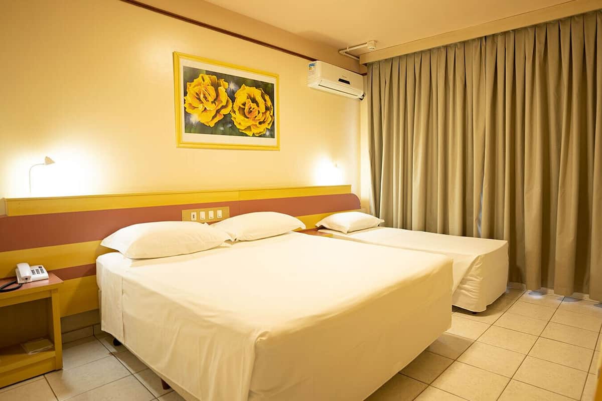 Ein Hotelzimmer mit zwei Betten, einem Gemälde von gelben Blumen an der Wand und einem Vorhang am Fenster.