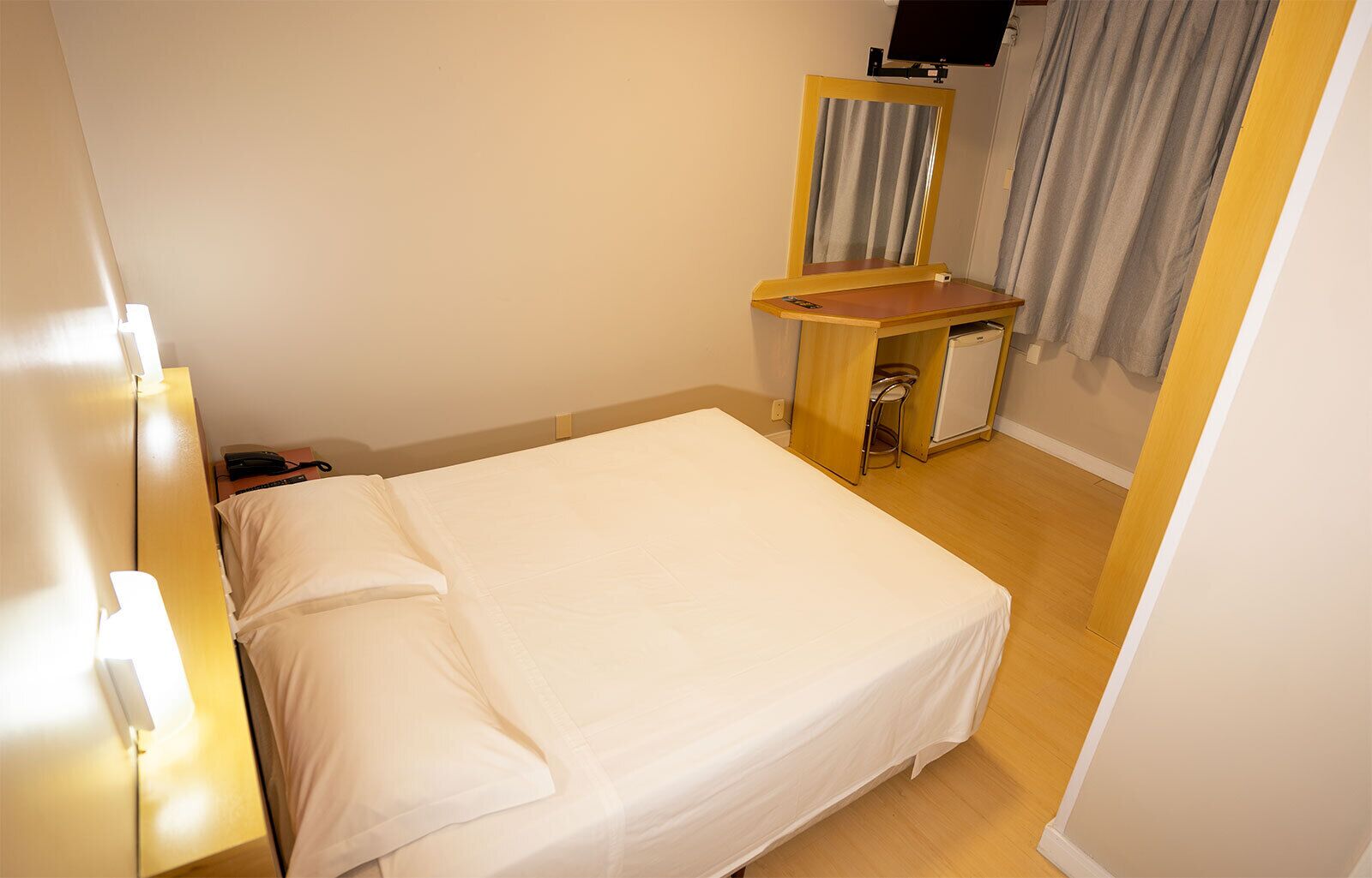 A hotel room with a bed, a desk, a chair, a TV, and a curtain.