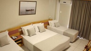 Una habitación de hotel con una cama grande, dos camas más pequeñas, una mesita de noche, un teléfono y un cuadro en la pared.
