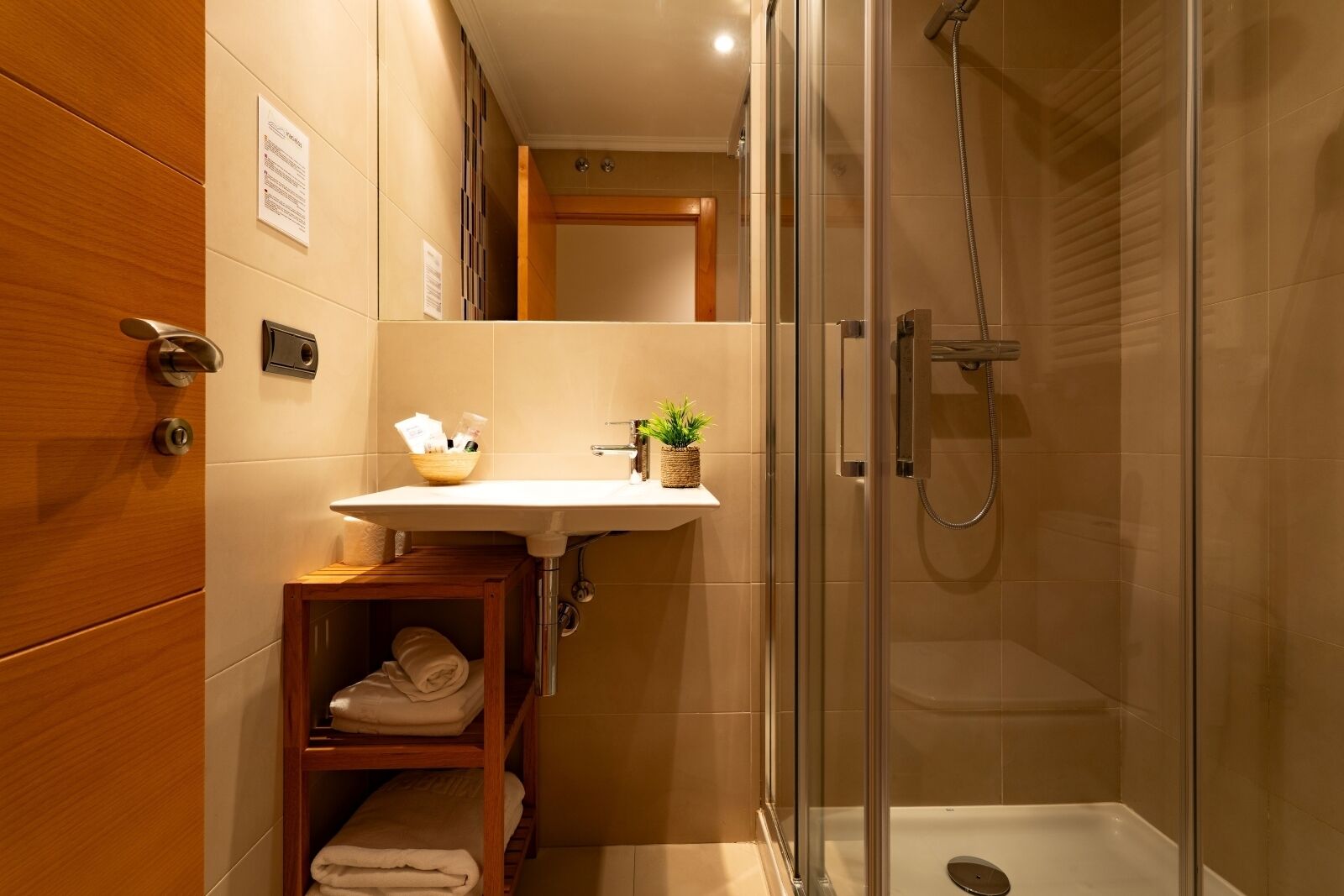 Un baño moderno con ducha envuelta en vidrio, tocador de madera y estante con toallas.
