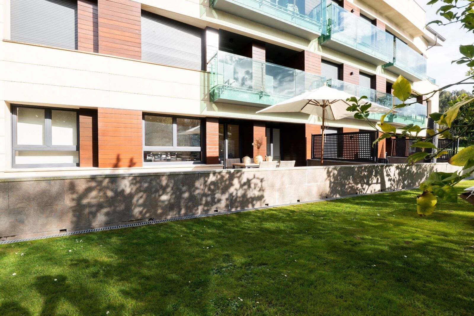 A modern multi-story residential building with balconies, large windows, and a well-maintained lawn.