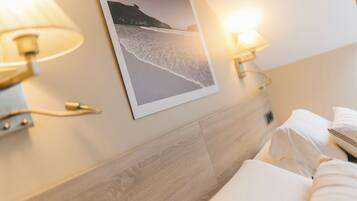 A hotel room with a wooden headboard, two wall-mounted lamps, and a framed photograph of a beach scene.