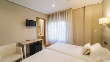 Habitación de hotel con dos camas, un escritorio, una silla, un televisor y una ventana con cortinas.