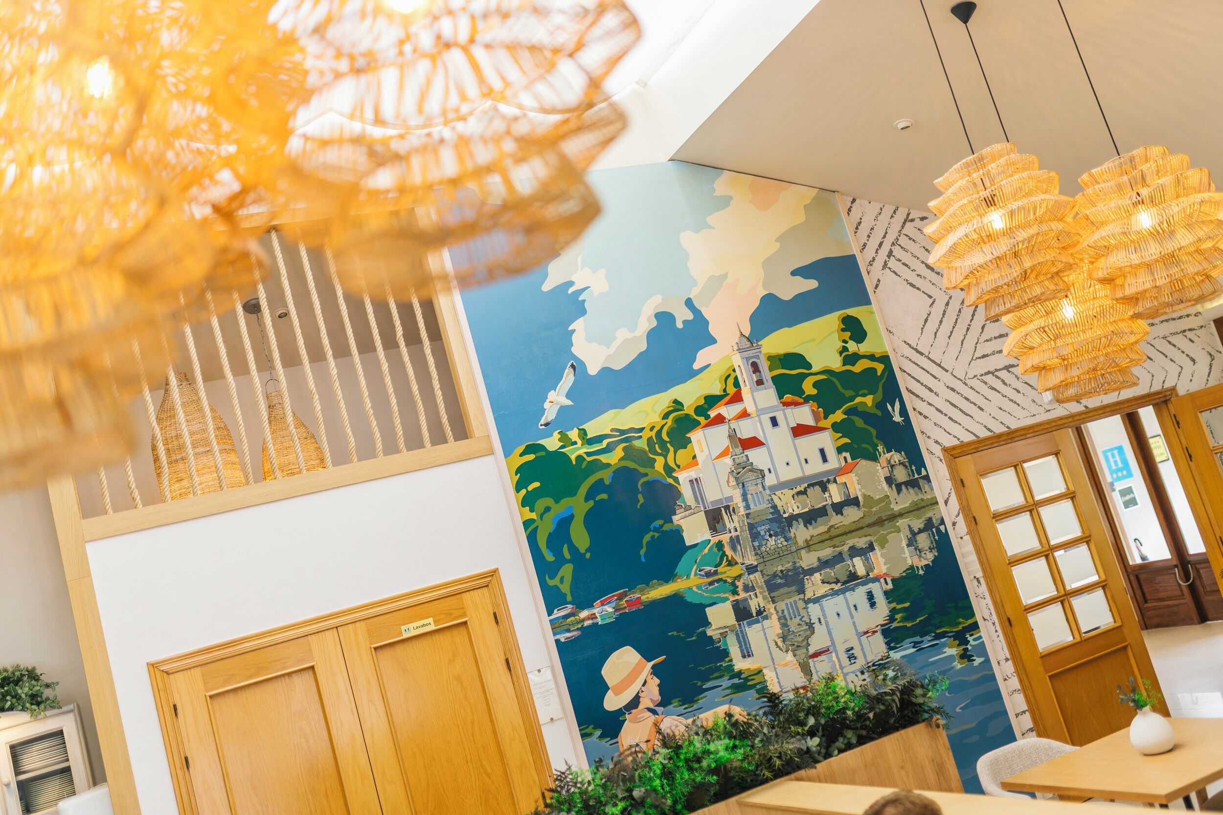 A hotel lobby with a mural of a coastal scene, wooden doors, and hanging light fixtures.