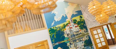 A hotel lobby with a mural of a coastal scene, wooden doors, and hanging light fixtures.