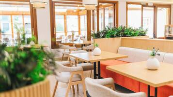 Un comedor moderno con mesas y sillas de madera, plantas en macetas y un interior luminoso.