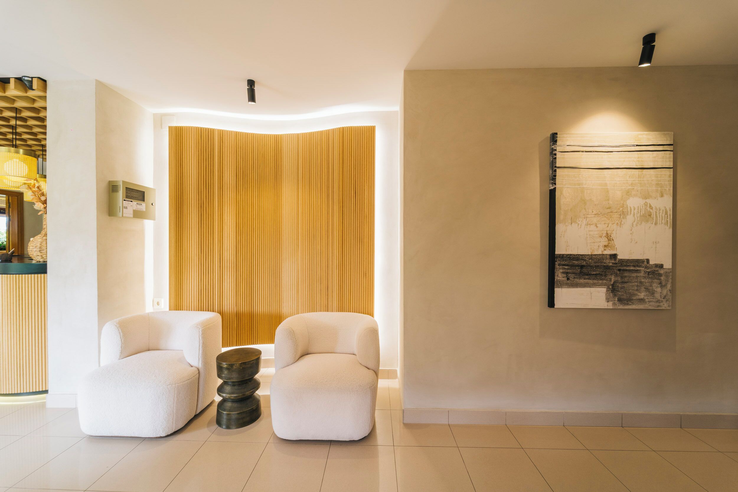 Un vestíbulo moderno con dos sillones blancos, un panel de pared de madera con listones, una obra de arte colgada en la pared y un mostrador de recepción.
