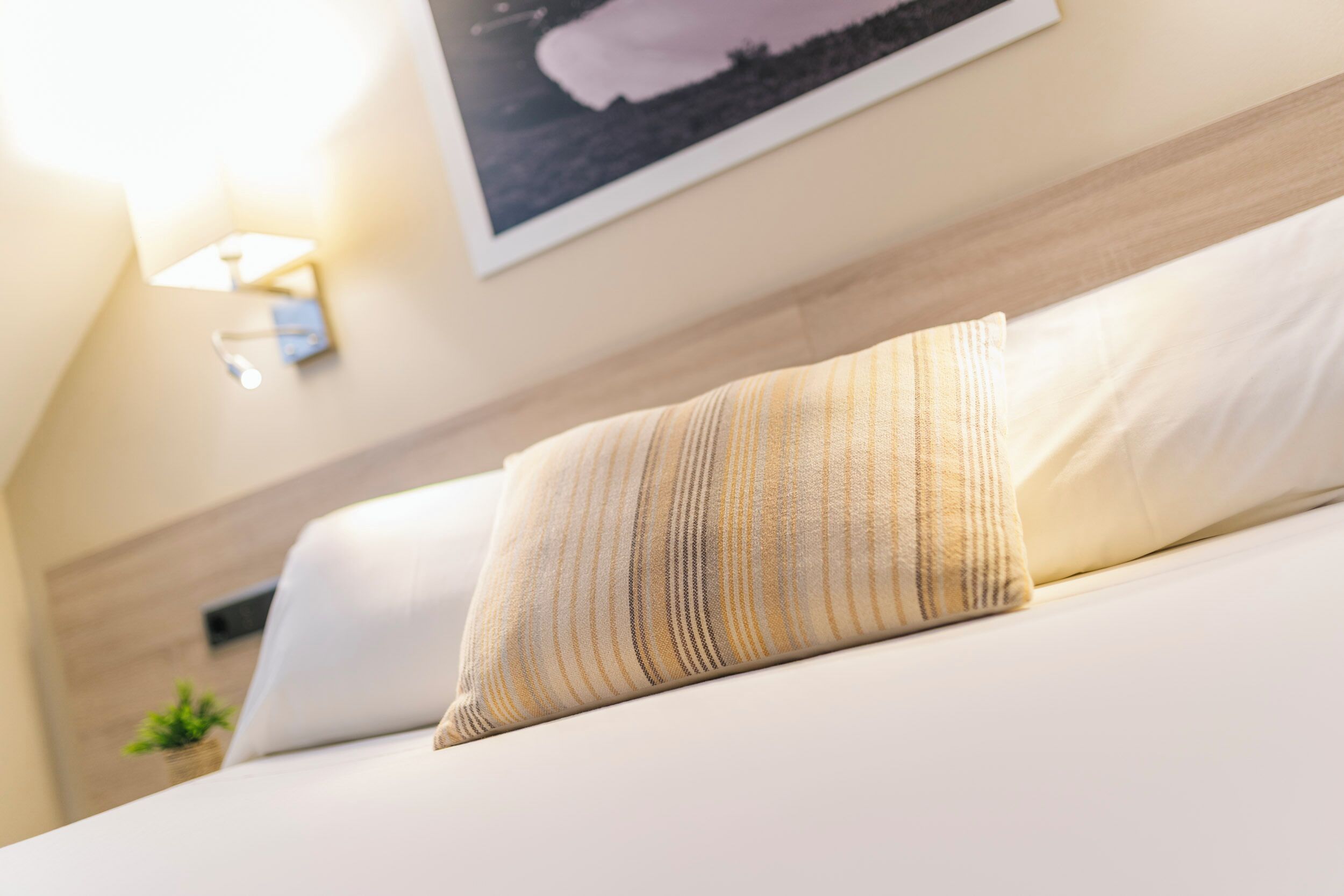 Una cama bien hecha con un cojín a rayas y una lámpara de pared.