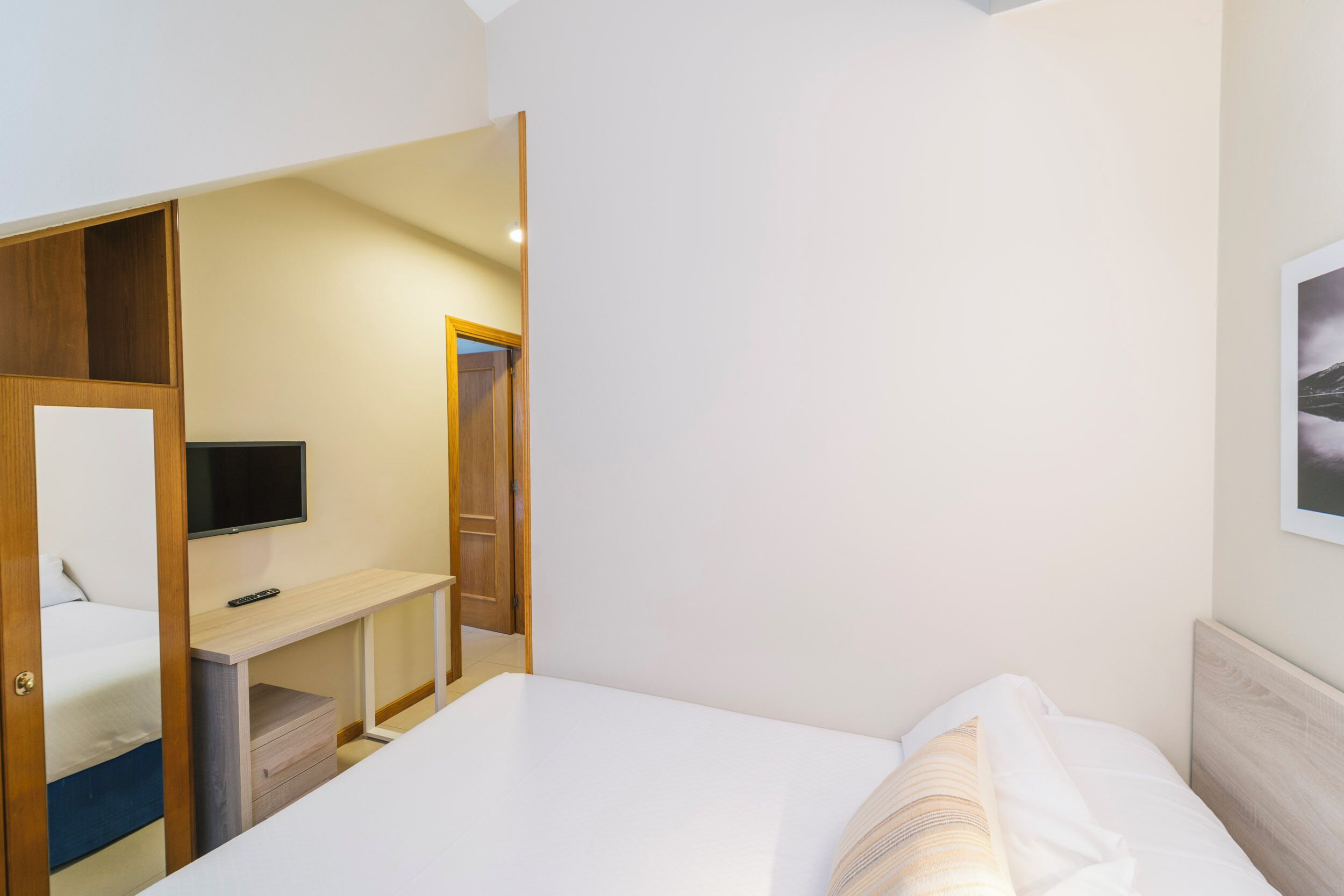 Ein Hotelzimmer mit Bett, einem an einer Holzwand montierten Fernseher, Schreibtisch und Kleiderschrank.