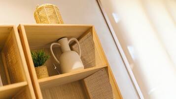 Una estantería de madera con una cesta tejida, una planta pequeña en maceta y una jarra blanca.