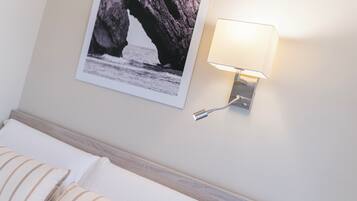 A hotel room with a bed, a wall-mounted lamp, and a framed picture of a coastal rock formation.