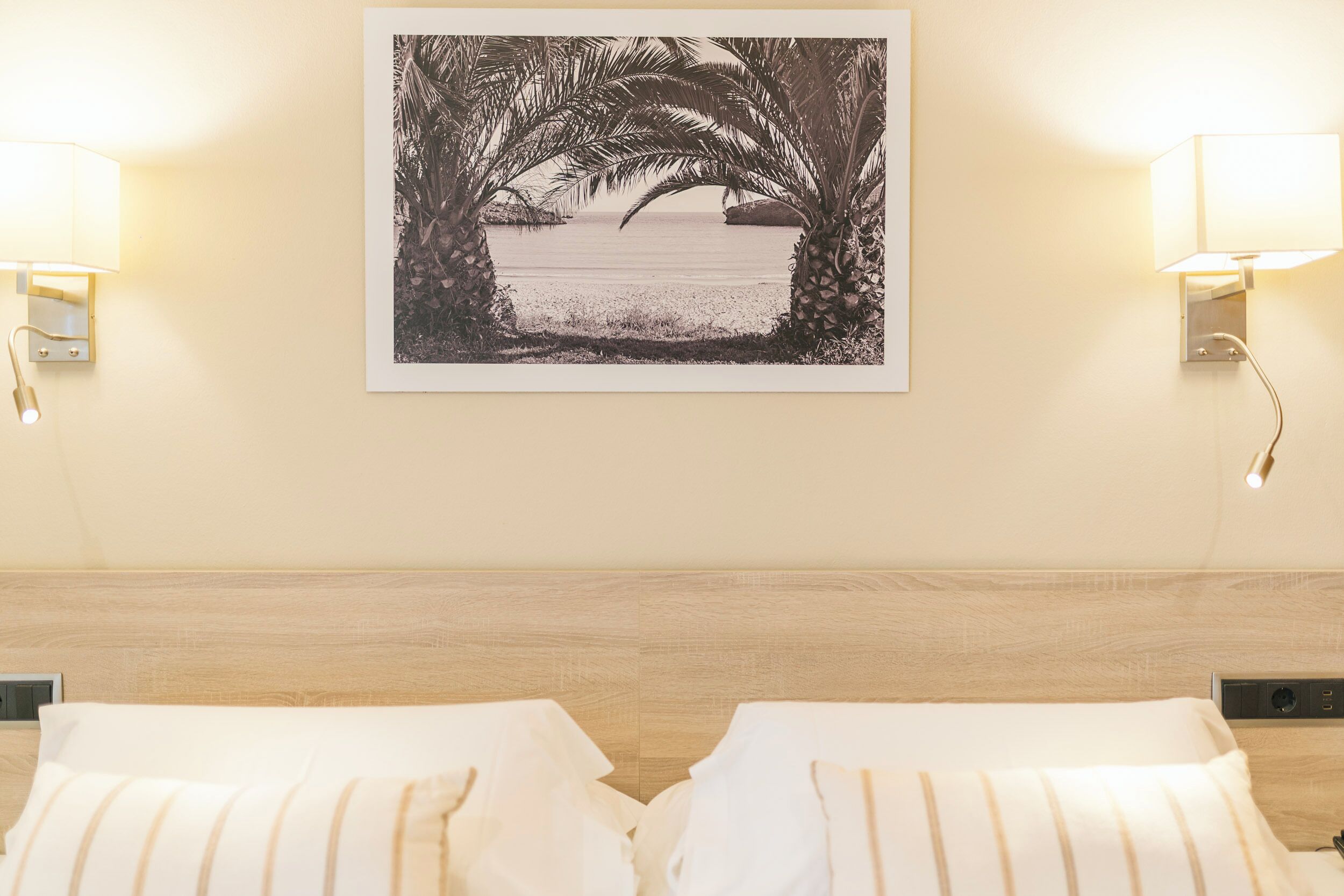 Habitación de hotel con cama, dos lámparas fijadas a la pared y un cuadro con una playa.