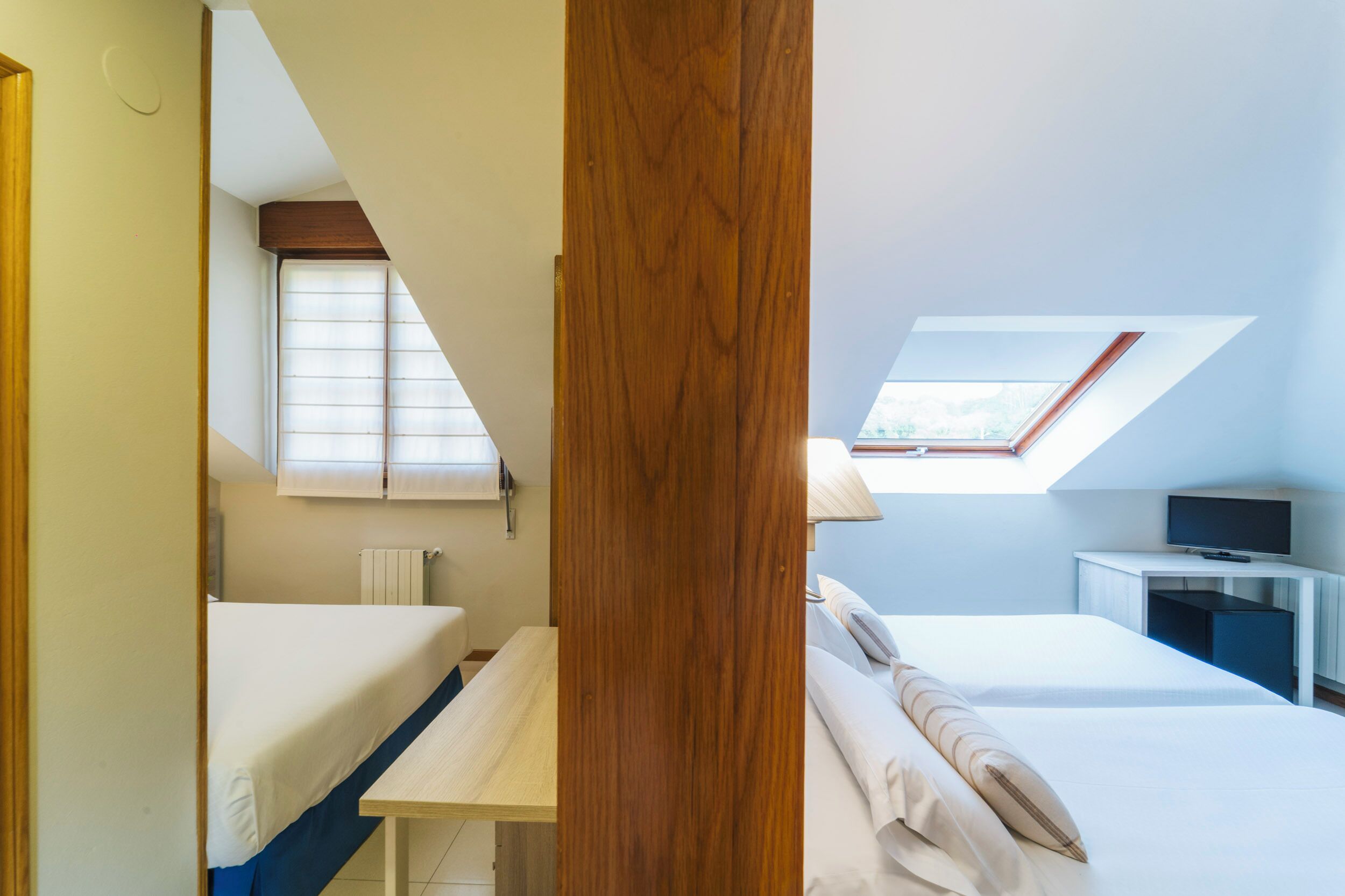 A bedroom with a skylight, a bed, a desk, and a television.
