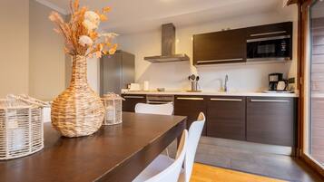 Una cocina moderna con armarios oscuros, una campana extractora de acero inoxidable y un microondas. Hay una mesa de comedor con sillas blancas y un jarrón tejido encima.