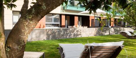Una hamaca bajo un árbol, una mesa de madera y un edificio con ventanas grandes y un balcón.