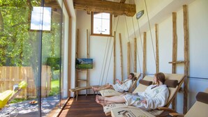 A spa room with wooden beams, glass walls, and a view of a garden. - Schloss Saalhof (Maishofen)