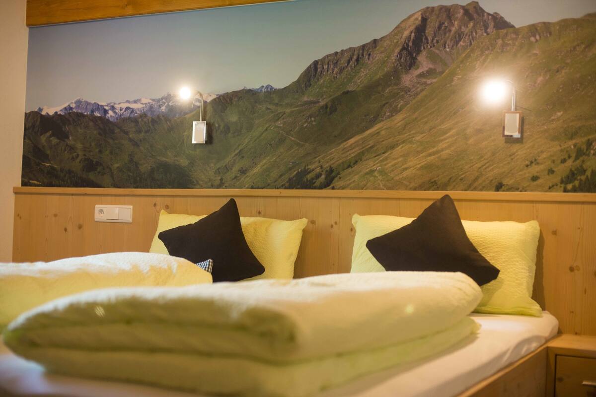 Une chambre d’hôtel avec un lit, des oreillers, une couverture et une fresque murale représentant un paysage de montagne.