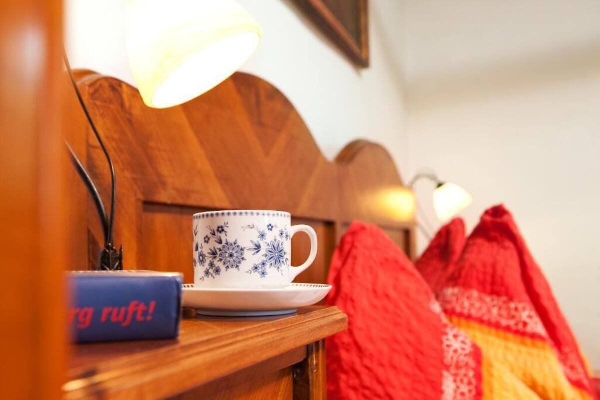 Une tête de lit en bois, une tasse et une soucoupe posées sur une table de chevet, une lampe et une couverture rouge.