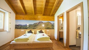 A wooden-framed bedroom with a mountain view mural, a double bed with pillows, and a bathroom with a sink and mirror. - Schloss Saalhof (Maishofen)