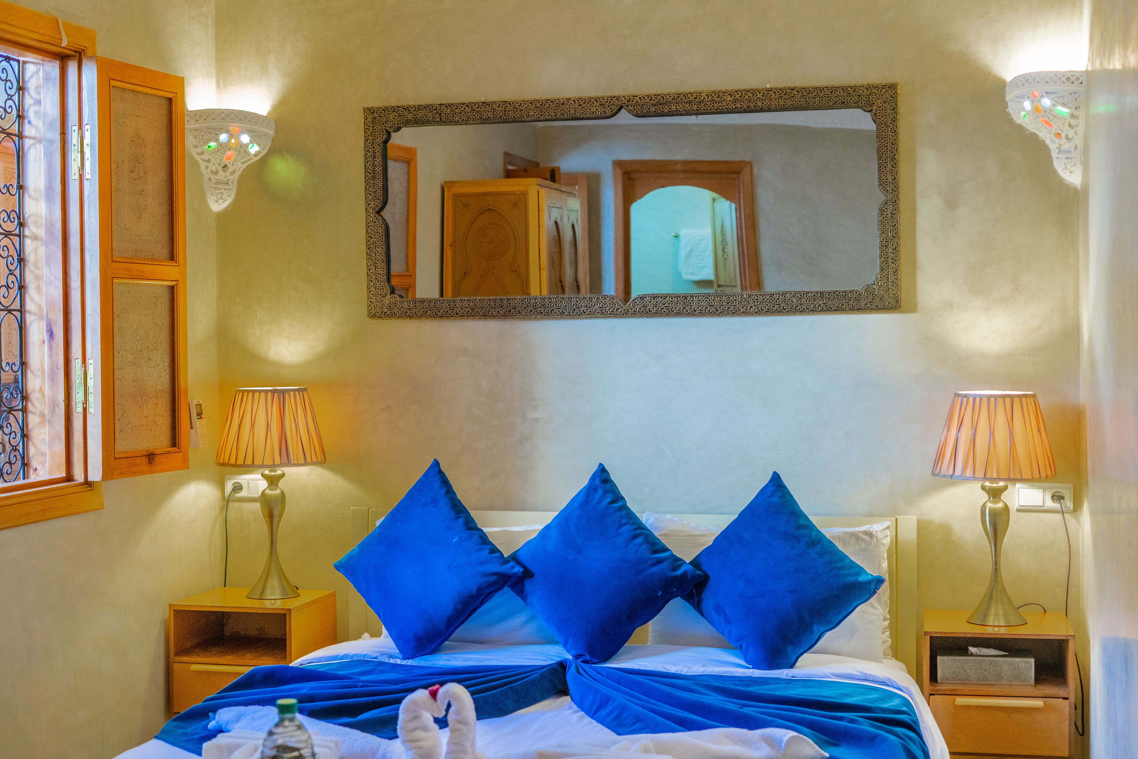 Habitación de hotel con cama, dos mesitas de noche, un espejo y una ventana con cortinas.