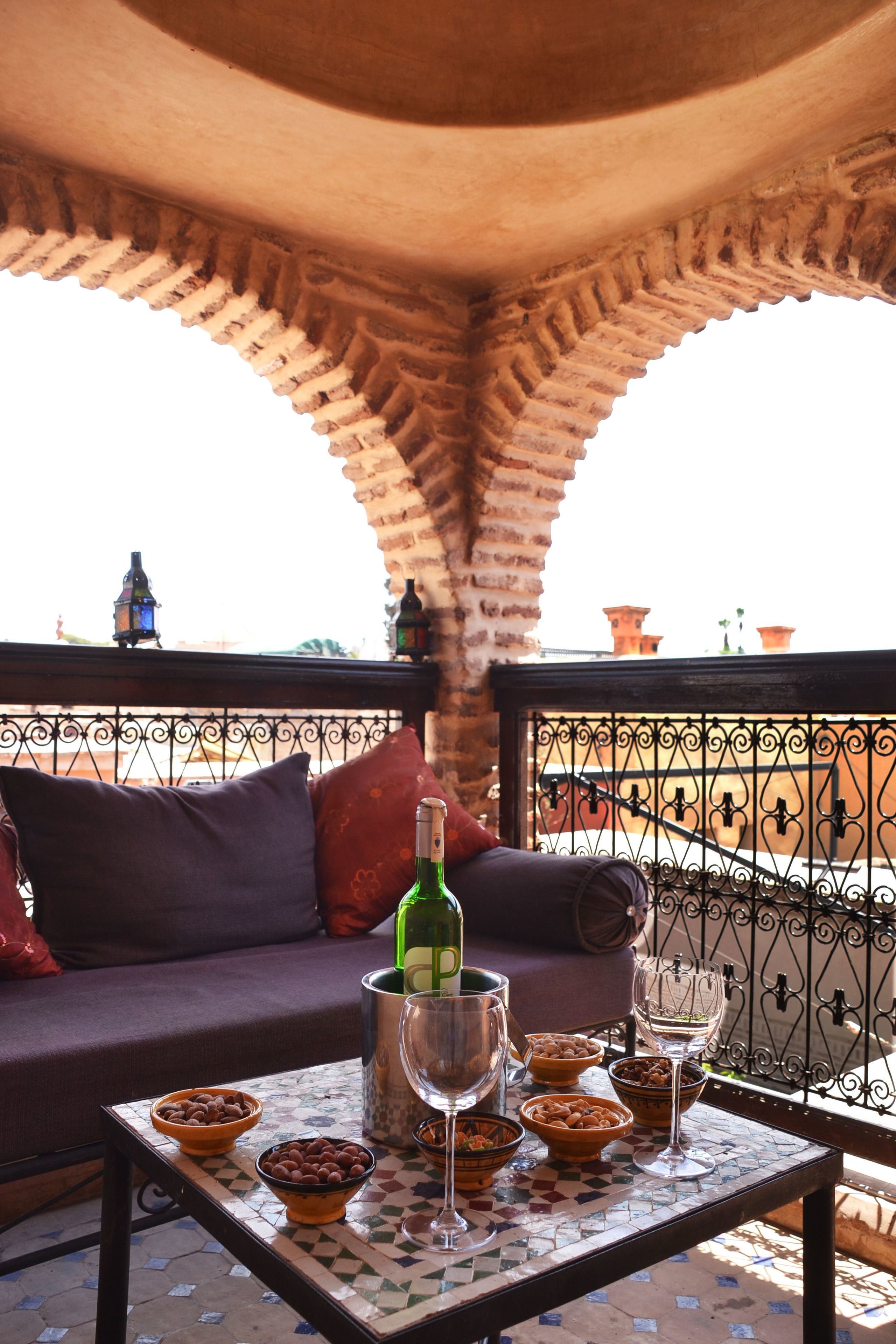 A terrace with a tiled table, bowls of snacks, a bottle of wine, and a sofa with cushions.