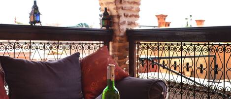A terrace with a tiled table, bowls of snacks, a bottle of wine, and a sofa with cushions.