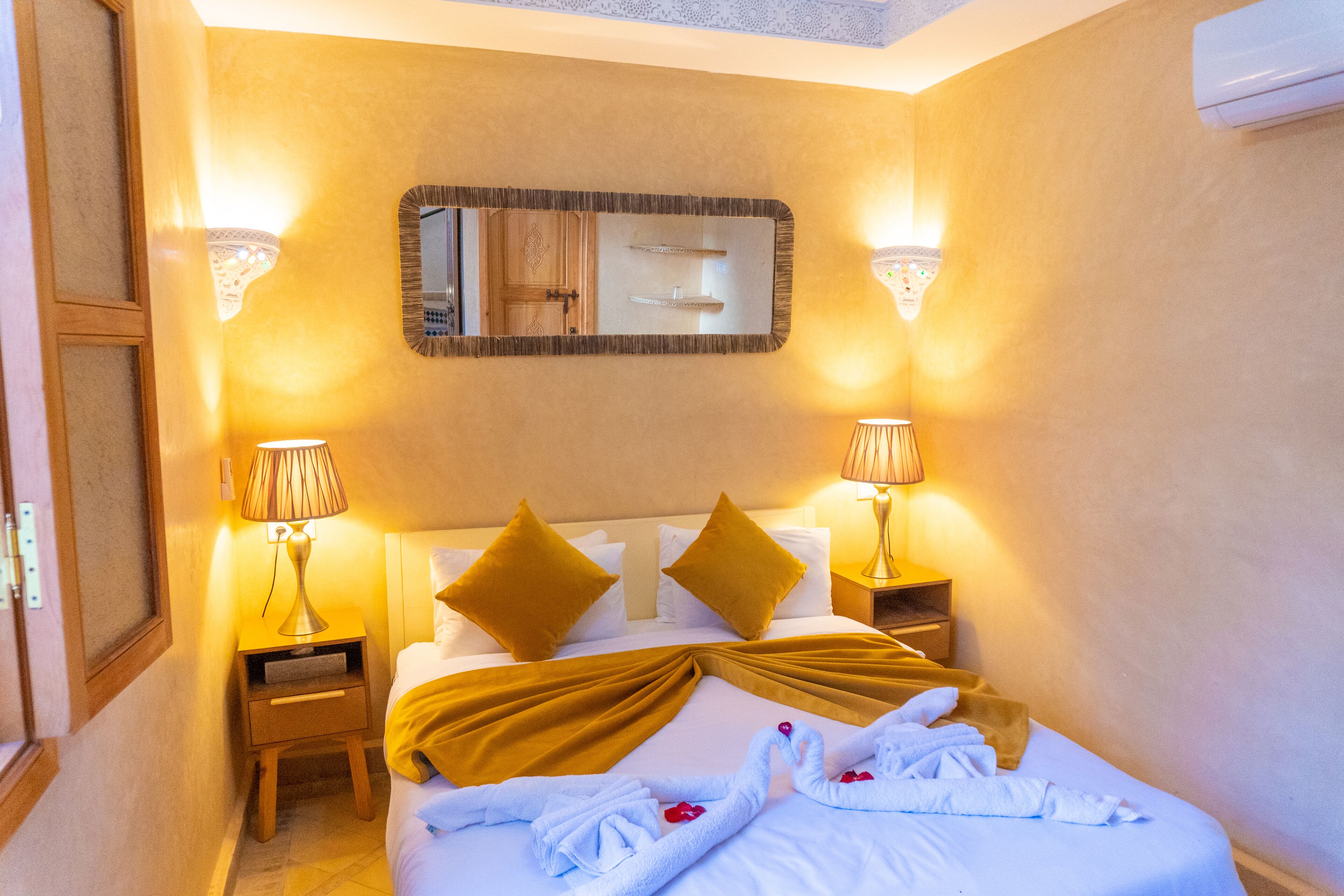 Una habitación de hotel con una cama bien hecha, dos lámparas de noche, un espejo y una mesita de noche de madera.