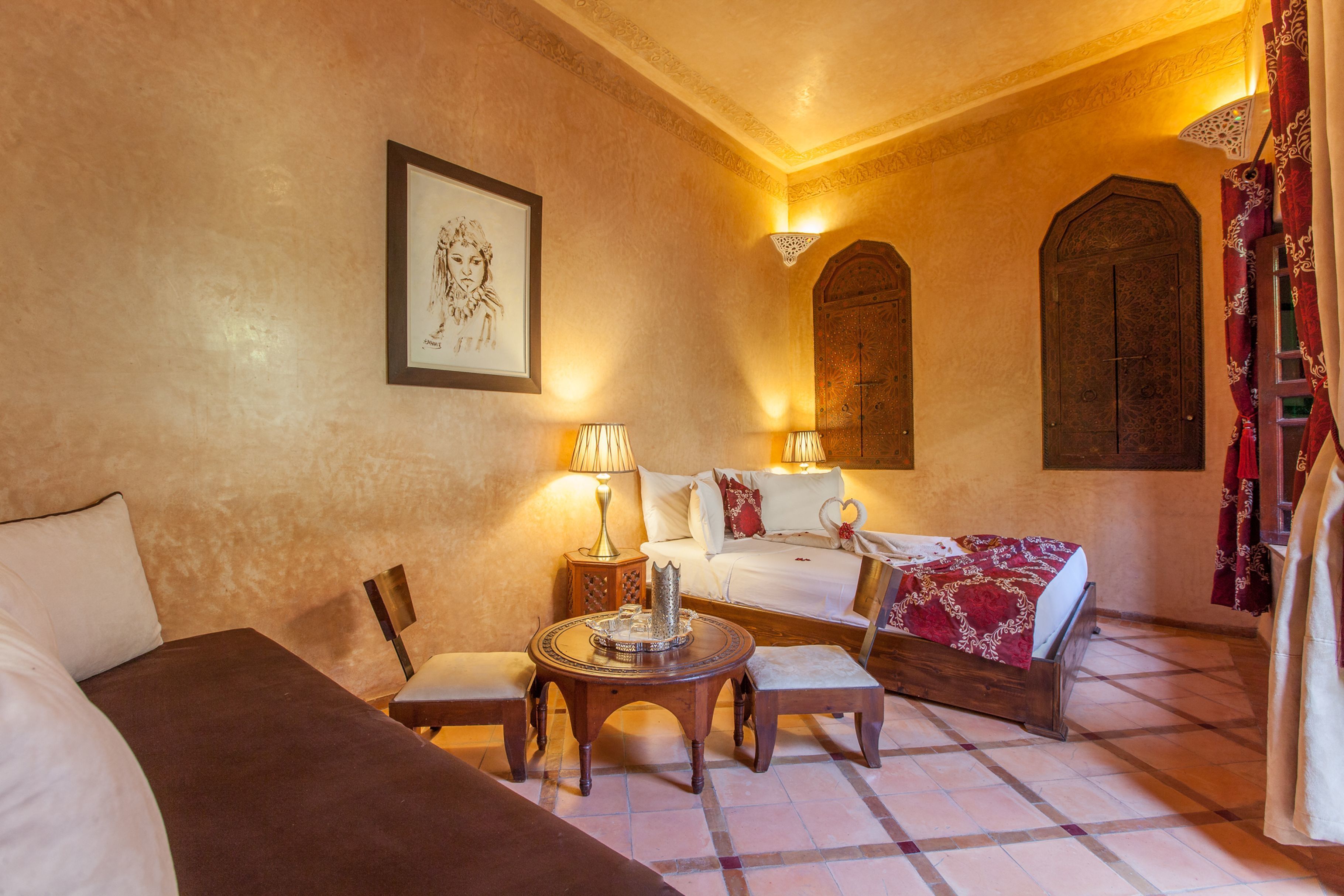 A hotel room with a bed, a sofa, a table, and a chair. There is a picture on the wall and a lamp on the table.