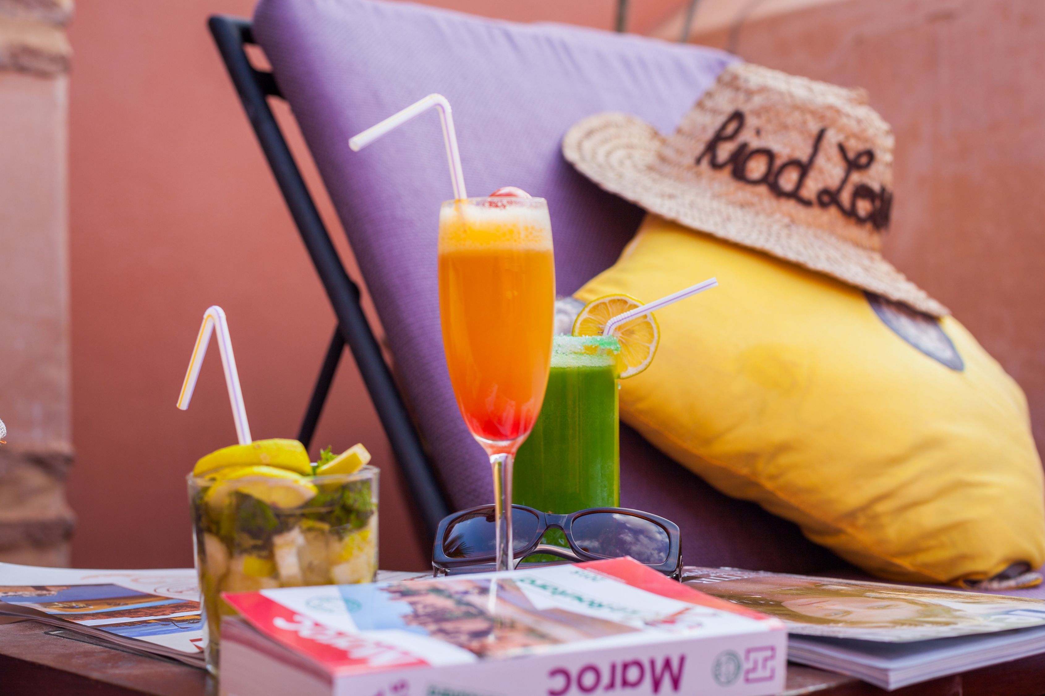 A table with two drinks, a pair of sunglasses, and a magazine.